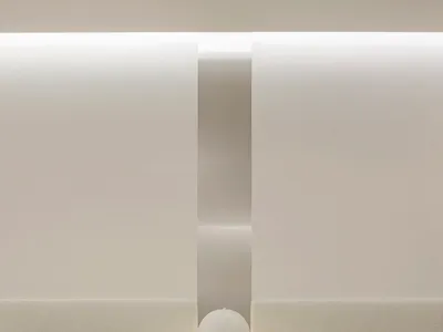 A minimalist restaurant interior with concrete and terrazzo surfaces and a blank white wall.
