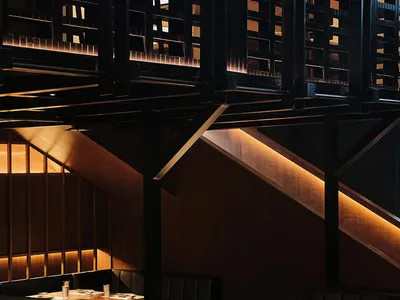 Interior of a modern restaurant featuring black furniture, wooden panels, and a warm, ambient lighting setup.