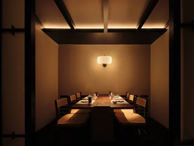 A modern restaurant dining room with a wooden table and chairs, set for dining with soft ambient lighting and minimalist deco