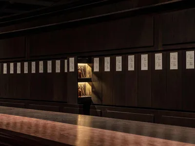 A dark wooden shelving unit in a restaurant bar with a hidden shelf illuminated from behind.