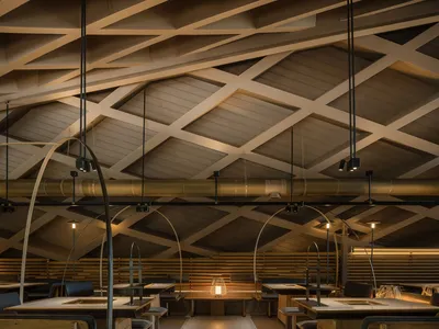 Industrial-style restaurant interior with wooden tables, arched ceiling, and hanging lights.