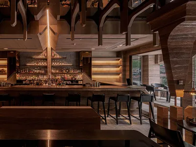 A modern restaurant bar with a wooden counter, metallic accents, and glass shelving.