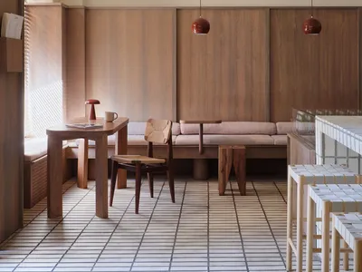 Modern restaurant cafe with wooden furniture, pendant lights, and a cushioned seating area.
