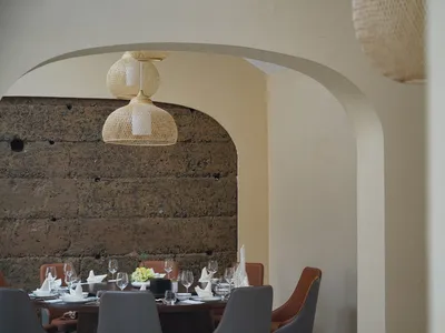Dining table set with wine glasses and tableware, under woven wood pendant lights in a restaurant interior.