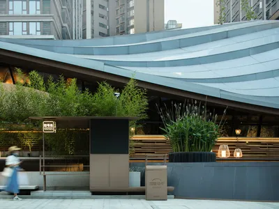 Modern restaurant exterior with metal roofing, planters, and lighting.