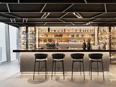 A sleek modern bar featuring glass shelves and metal stools.