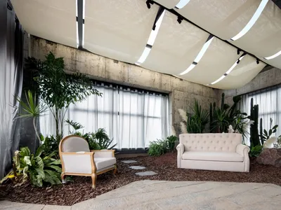Modern industrial living room featuring concrete walls and ceiling, large windows, and lush greenery.