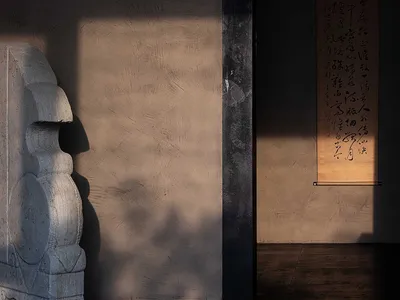 A minimalist bedroom decorated with a large concrete sculpture and a framed calligraphy scroll hanging on the wall.