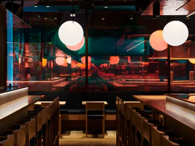 Modern restaurant interior with wooden benches, marble tables, and glass walls.