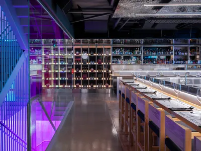 A modern restaurant interior featuring glass walls, concrete flooring, and wooden seating.