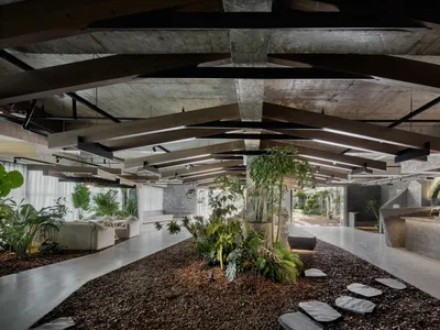 Modern industrial restaurant interior with concrete flooring, exposed wooden beams, and potted plants.