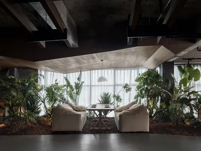 An indoor restaurant interior featuring concrete walls, wooden furniture, and lush green plants.