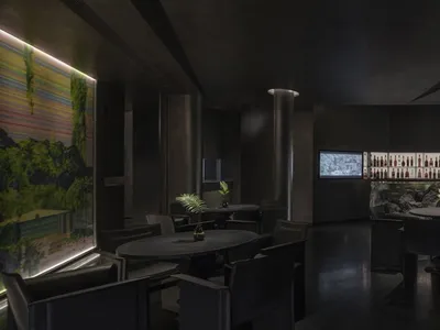 Modern restaurant bar featuring a black metallic wall, sleek furniture, and a display of bottled beverages and green plants.