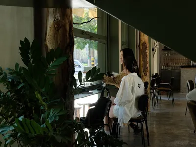 People sitting in a modern cafe interior with wooden tables and greenery.