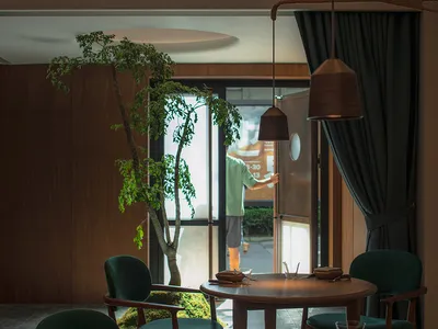 A cozy cafe interior with wooden tables and chairs, plants, and warm lighting.