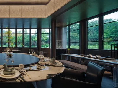 A round dining table with marble tabletop surrounded by black leather chairs, set with white plates and wine glasses.