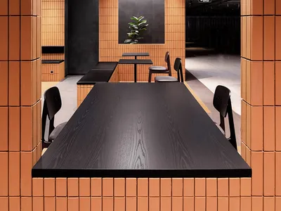 Minimalist restaurant interior with clay tiles, black wooden tables, and a green plant.