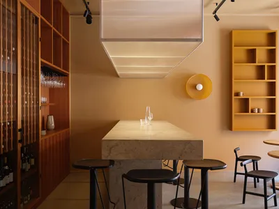 A modern restaurant interior with concrete tables, wooden shelves, and leather stools.