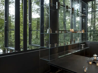 A minimalist restaurant interior with glass walls and wooden accents, featuring sleek metal furniture and a large display cas