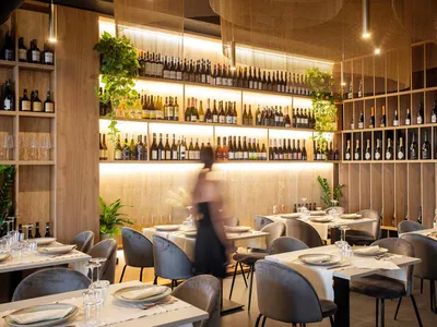 A beautifully designed restaurant interior with wooden walls, glass shelving, metal furniture, and green plants.