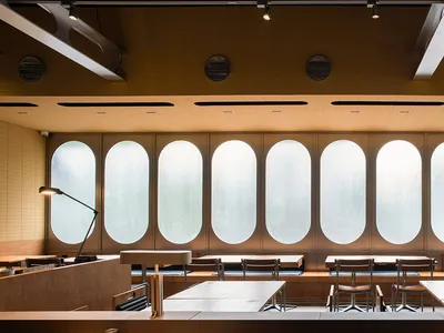 Industrial-style restaurant interior with wooden tables, metal railings, and large oval windows.