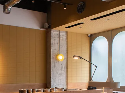 Modern industrial restaurant interior featuring wooden tables, metal stools, and concrete walls with exposed pipes and lighti