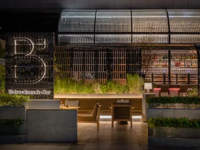 Interior view of a modern restaurant and bar with glass walls, concrete seating, and modern decor.