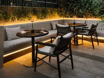 A modern restaurant exterior with concrete and glass materials, featuring outdoor seating area and urban background.