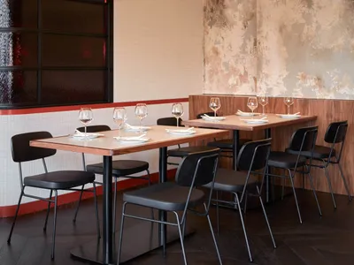 Modern restaurant dining area with wooden tables, metal chairs, and glass windows.