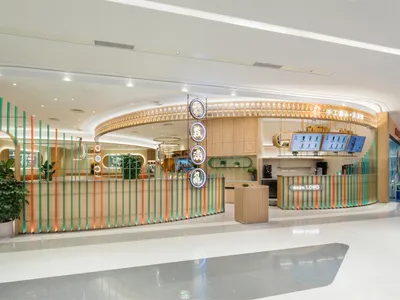 A modern restaurant entrance featuring a curved wooden counter with colorful vertical structures and digital displays.