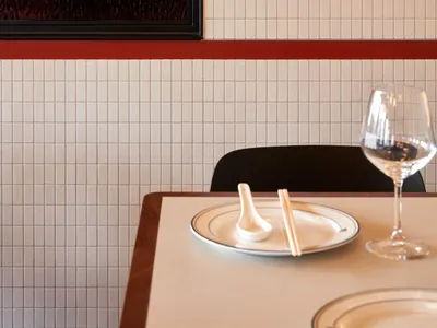 A minimalist-style restaurant interior with tile walls and a wine glass on a table.