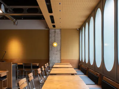 Modern restaurant interior with wooden tables, concrete walls, and glass windows