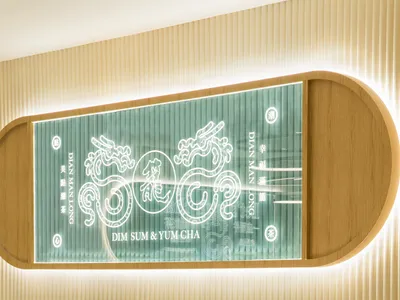 Modern restaurant interior with wooden furniture, seating arrangements, and a glass wall displaying the restaurant's name and