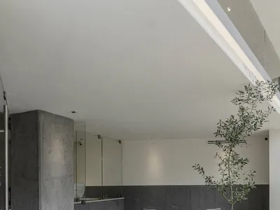 Modern, minimalist restaurant interior with concrete flooring and walls, white furniture, and greenery.