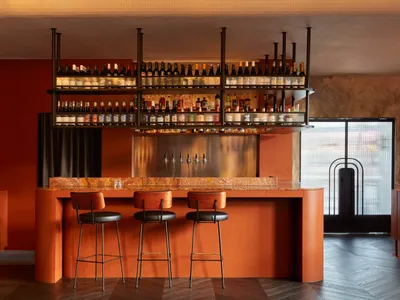 A photograph of a modern restaurant bar featuring red wooden stools and a marble countertop.