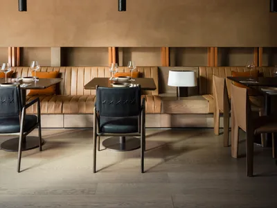 A modern restaurant interior with plush leather seating, wooden dining tables, and sleek black pendant lights.