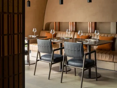 Modern restaurant interior featuring leather seating, wooden tables, and concrete walls.