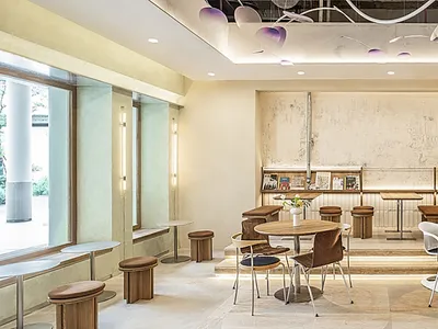 A casual café interior with wood tables, metal stools, and plaster walls.