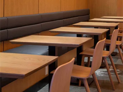 Modern restaurant dining area with wooden tables, chairs, and a wood-paneled wall with recessed lights.
