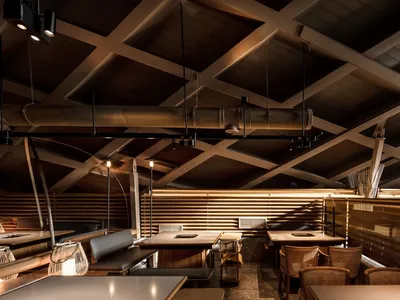 A modern restaurant interior with wooden tables, metal chairs, and concrete floors.