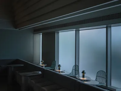 A minimalist restaurant interior featuring metallic furniture and large glass windows.