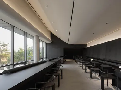 Interior of a modern restaurant with black and concrete elements, featuring minimalist design.
