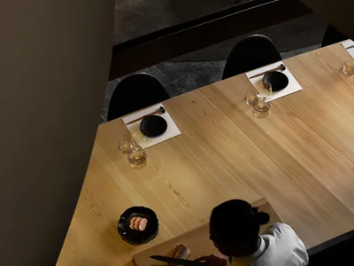 A minimalist restaurant interior with a wooden counter and a chef slicing fish.