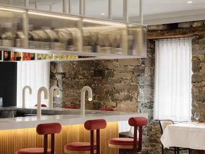 A modern restaurant bar featuring wood, glass, and stone materials with stylish red bar stools.