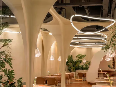 Modern restaurant interior with concrete walls, floral decor, and glass hanging lights.