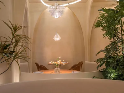 A high-end restaurant interior featuring smooth, neutral-toned walls and archways, with a round table and chairs set in the c