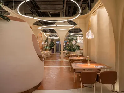 A modern restaurant interior with a terrazzo floor and concrete pillars adorned with green plants.