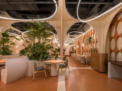 A modern restaurant interior with concrete finishes and white planters filled with greenery.