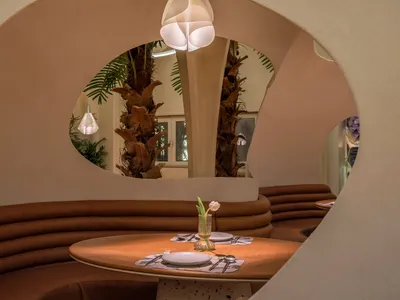 A modern restaurant setting featuring a round table with white plates, silverware, and a single white tulip in a vase, surrou