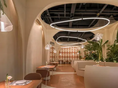 A modern restaurant interior with neutral-colored decor and arch-shaped ceiling lights.